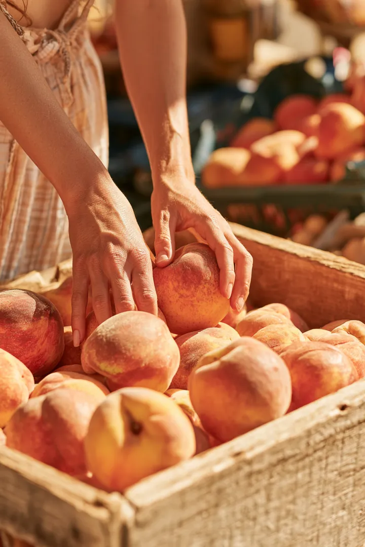 Hands choosing ripe peaches from a crate at a farmers market